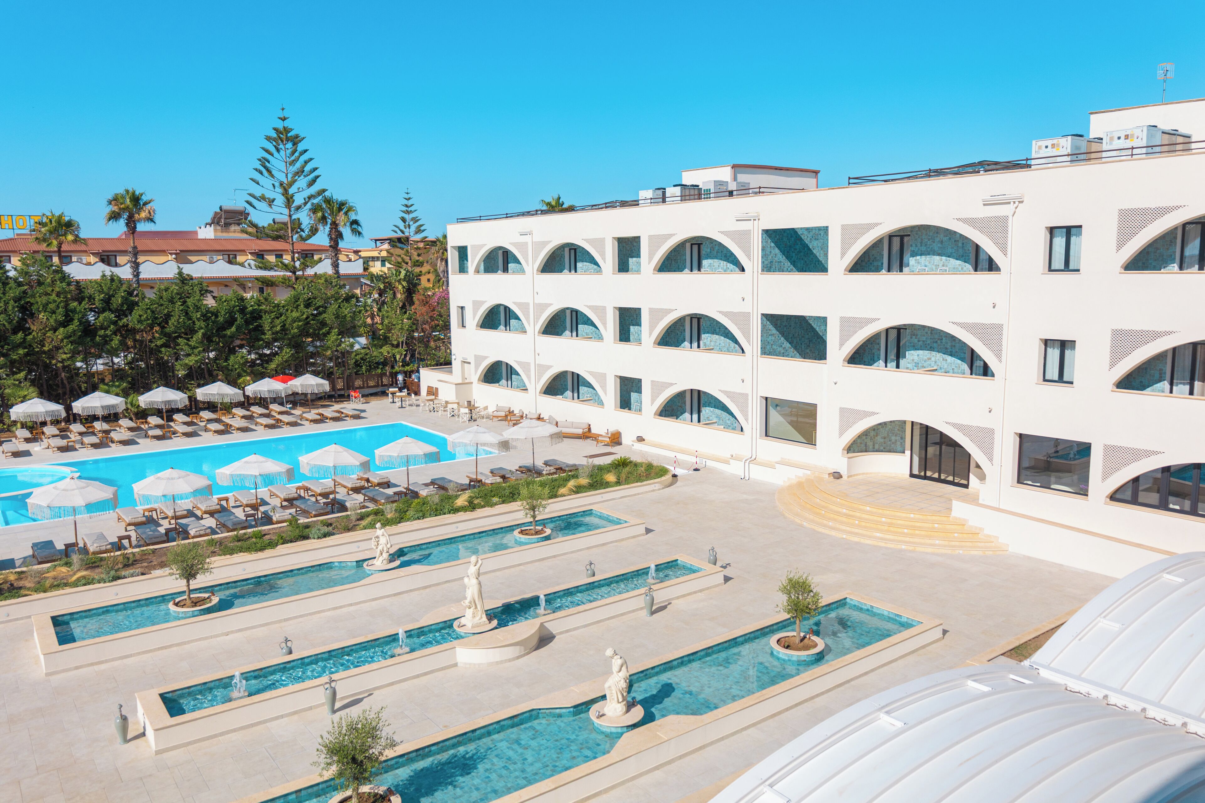 A hotel with multiple swimming pools, sun loungers, and umbrellas.