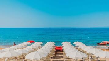 A beach with rows of white umbrellas and chairs, a red boat, and the sea in the background.