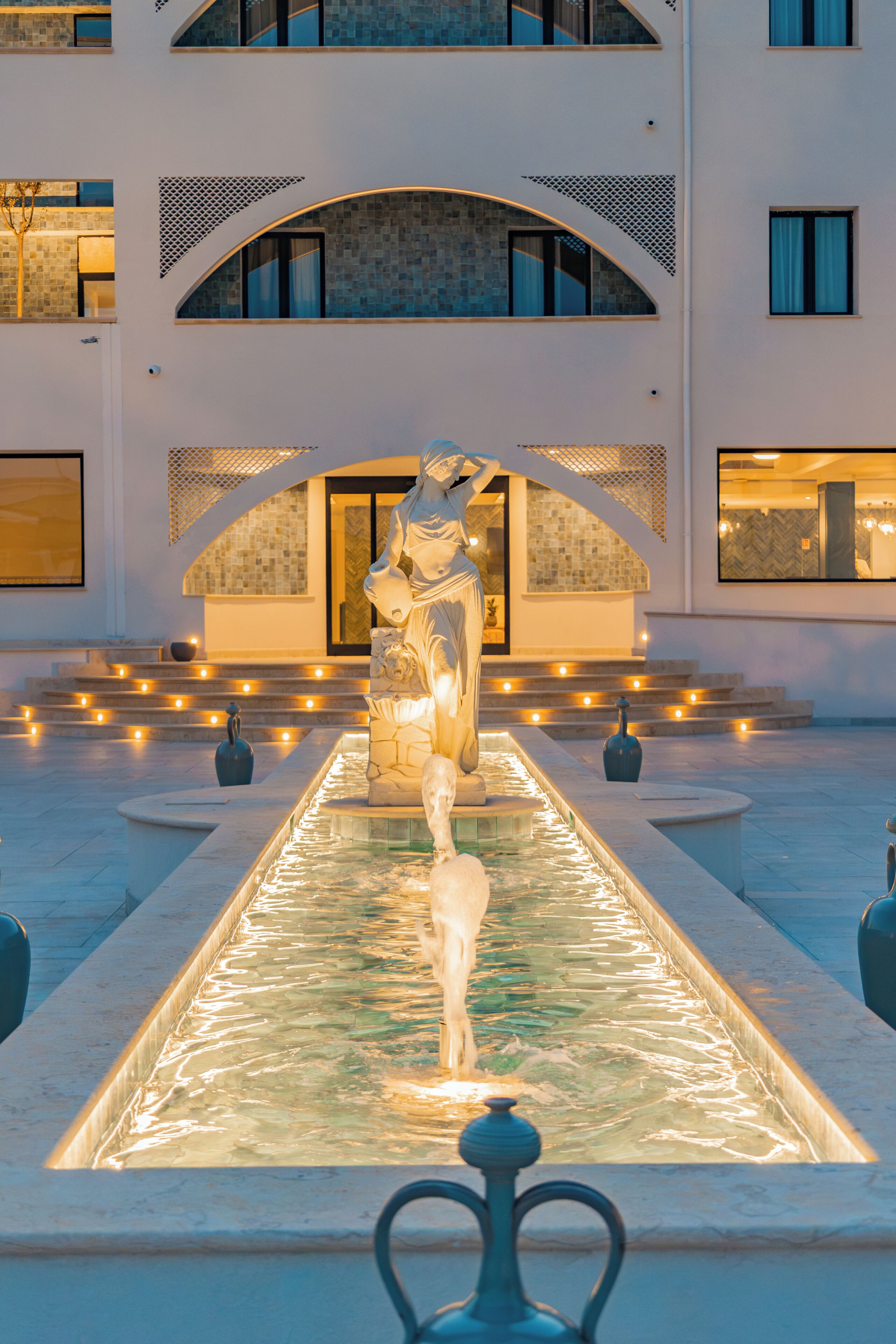Un edificio con un patio central que presenta una estatua, una fuente y una zona de estar.