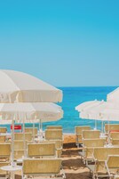 Zona relax in spiaggia con ombrelloni bianchi e sedie in vimini, vista sull'oceano.
