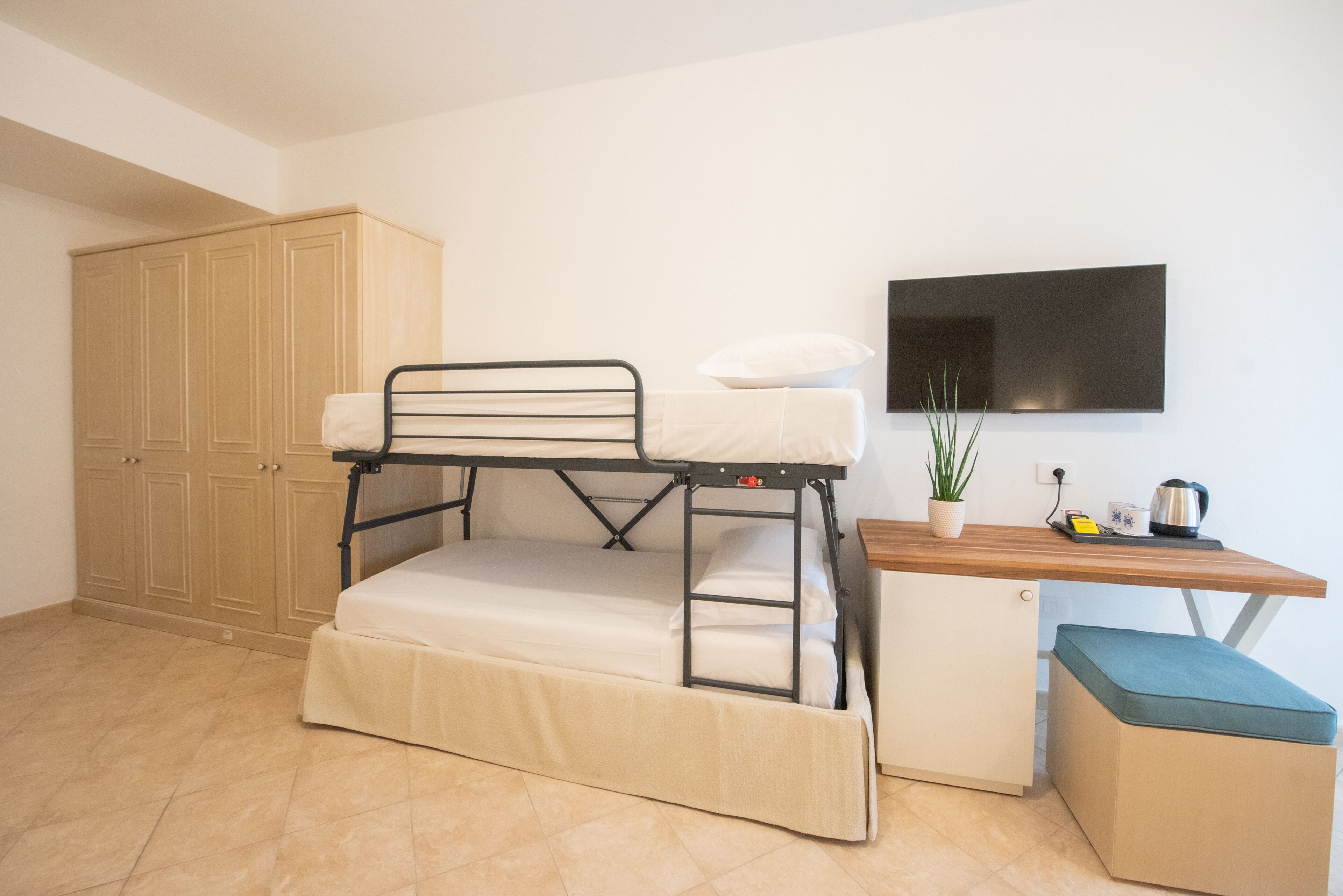 Un lit superposé avec un bureau et un téléviseur dans une pièce qui comprend également une armoire et une plante en pot.