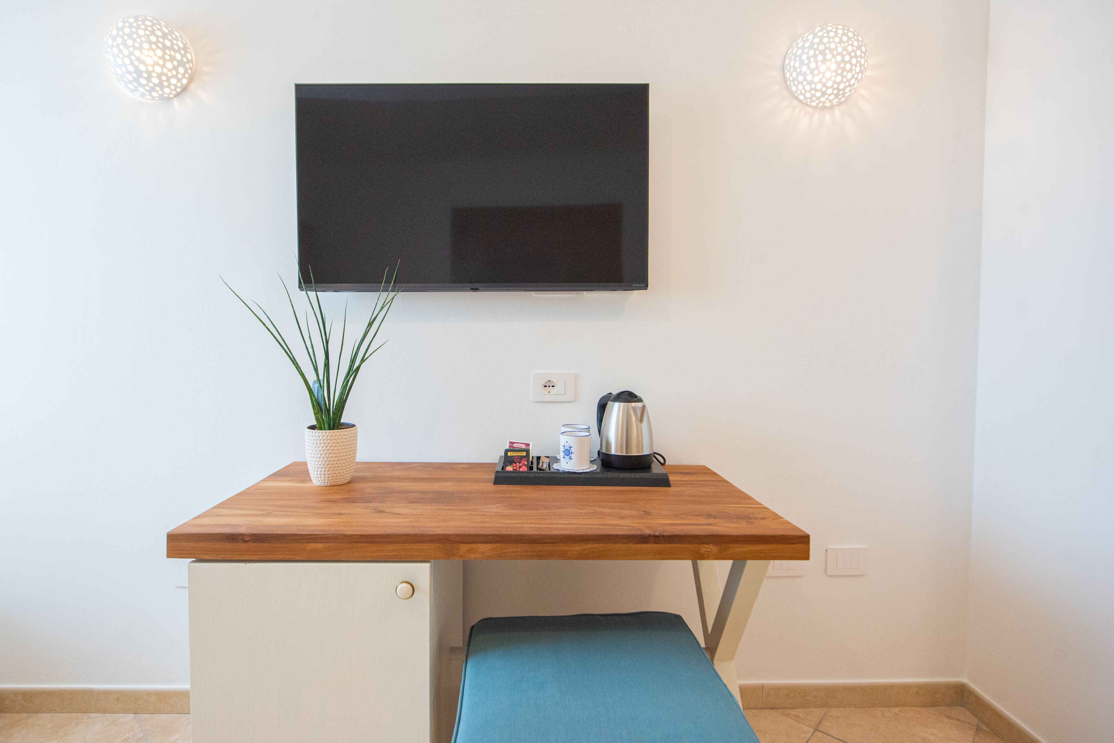 Een compacte kitchenette met een houten aanrecht, een televisie erboven, een bloempot en een waterkoker.