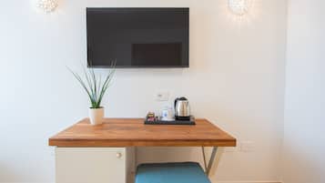 Een compacte kitchenette met een houten aanrecht, een televisie erboven, een bloempot en een waterkoker.