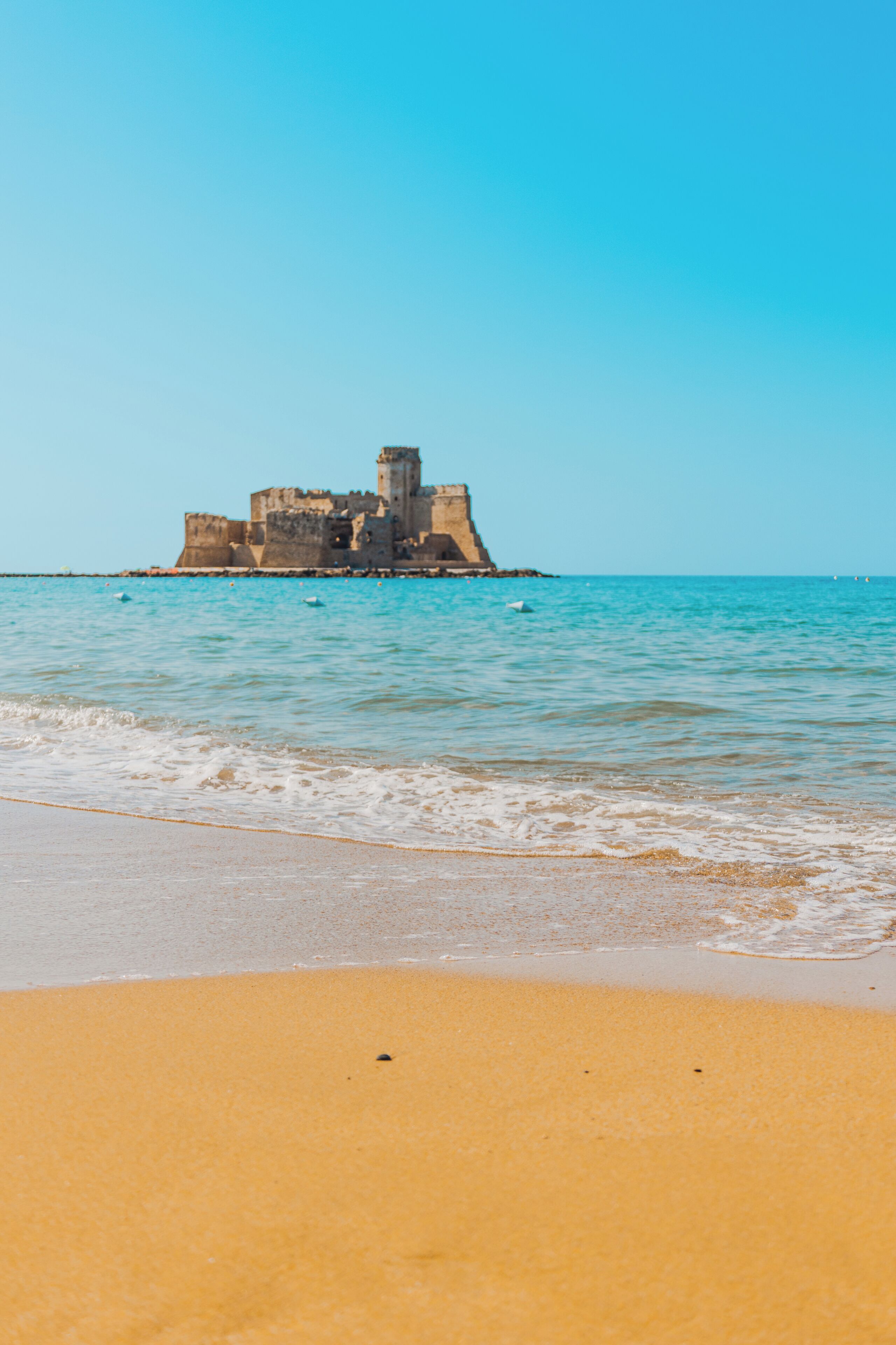 A sandy beach with a historic stone structure in the water.