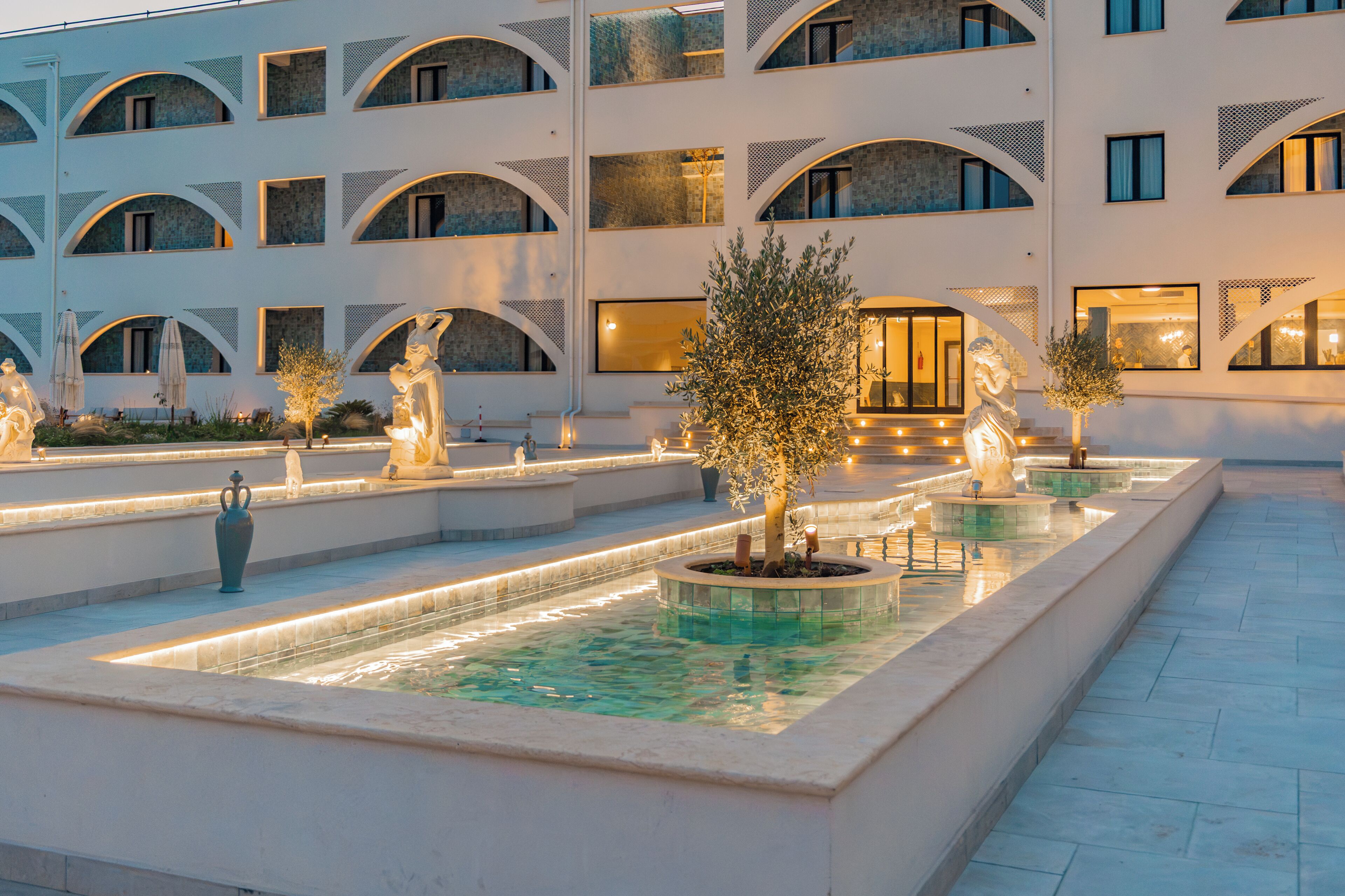 Un patio con una fuente, estatuas y un edificio con varios balcones.