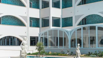 A modern building with multiple balconies, a swimming pool, and classical statues.