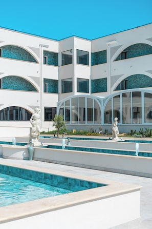 A modern building with multiple balconies, a swimming pool, and classical statues. - CDSHotels Le Castella - Ninfe Saracene (Le Castella)