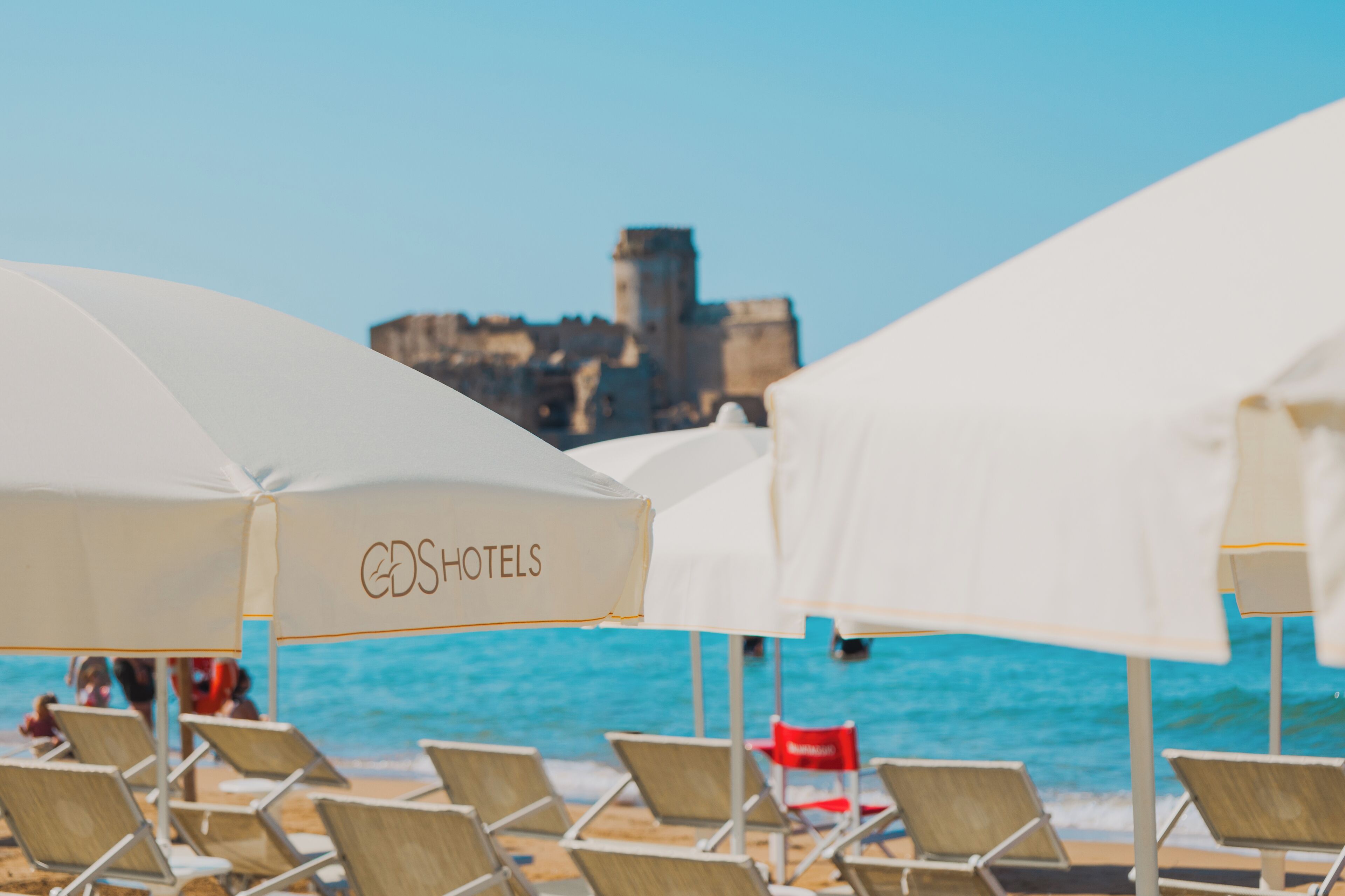 A beach with rows of white umbrellas labeled 'CDSHOTELS' and beach chairs.