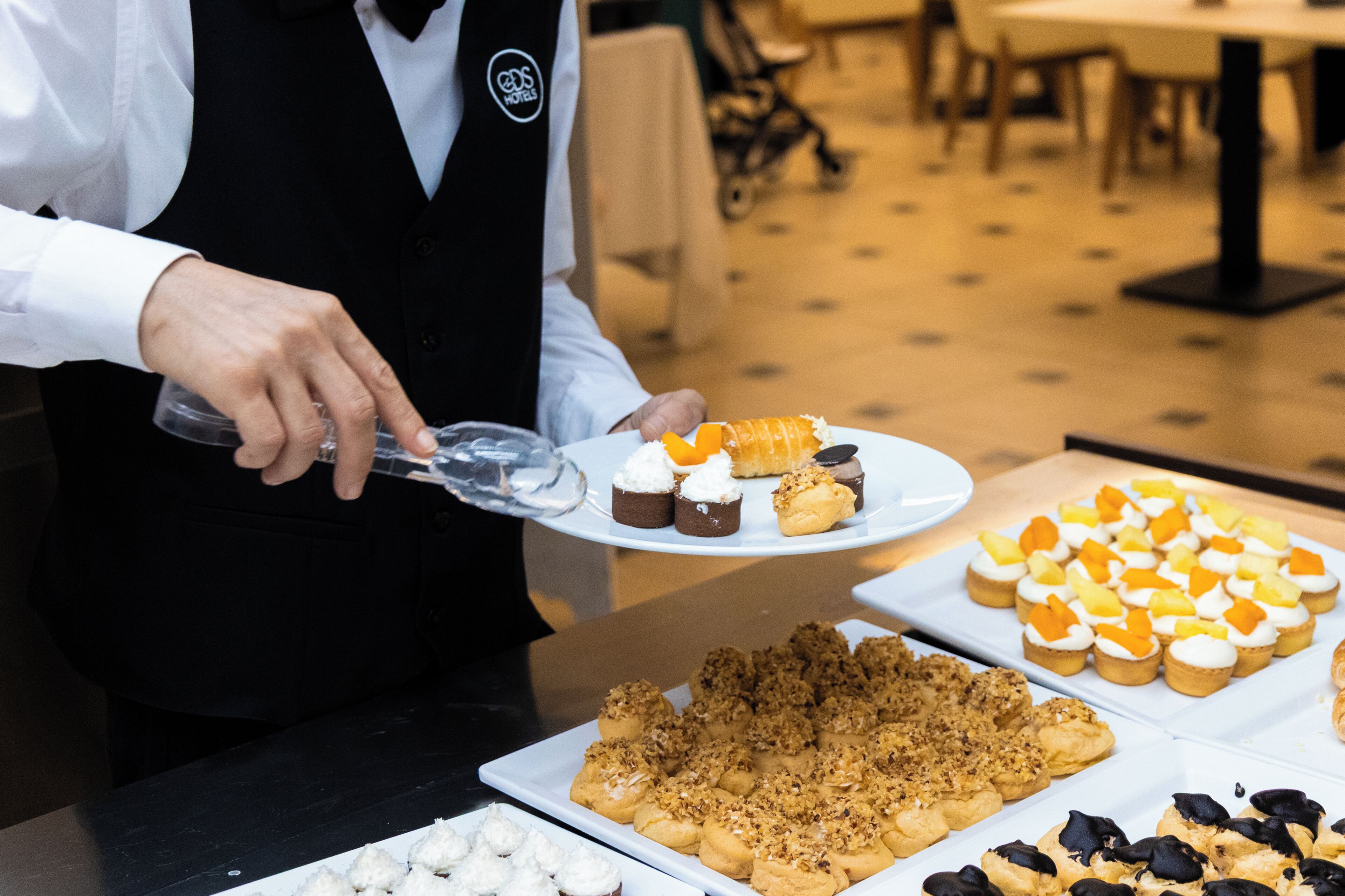 A person serving food at a buffet with various desserts and pastries on display.