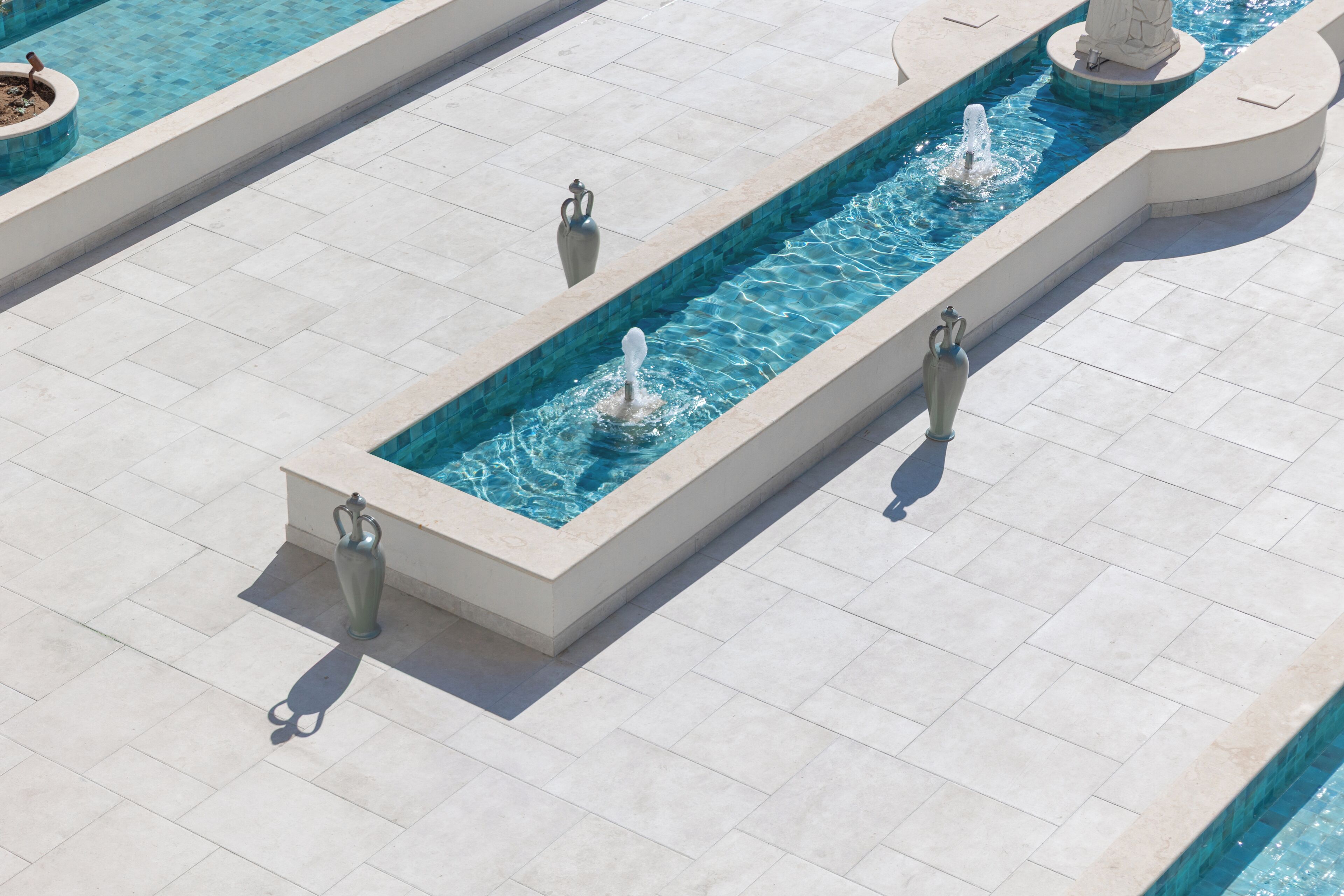 A rectangular water feature with multiple fountains, surrounded by a tiled walkway.