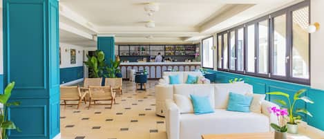 Un hall d’hôtel doté d’un bar, de différents espaces aménagés pour s’asseoir et de grandes fenêtres.