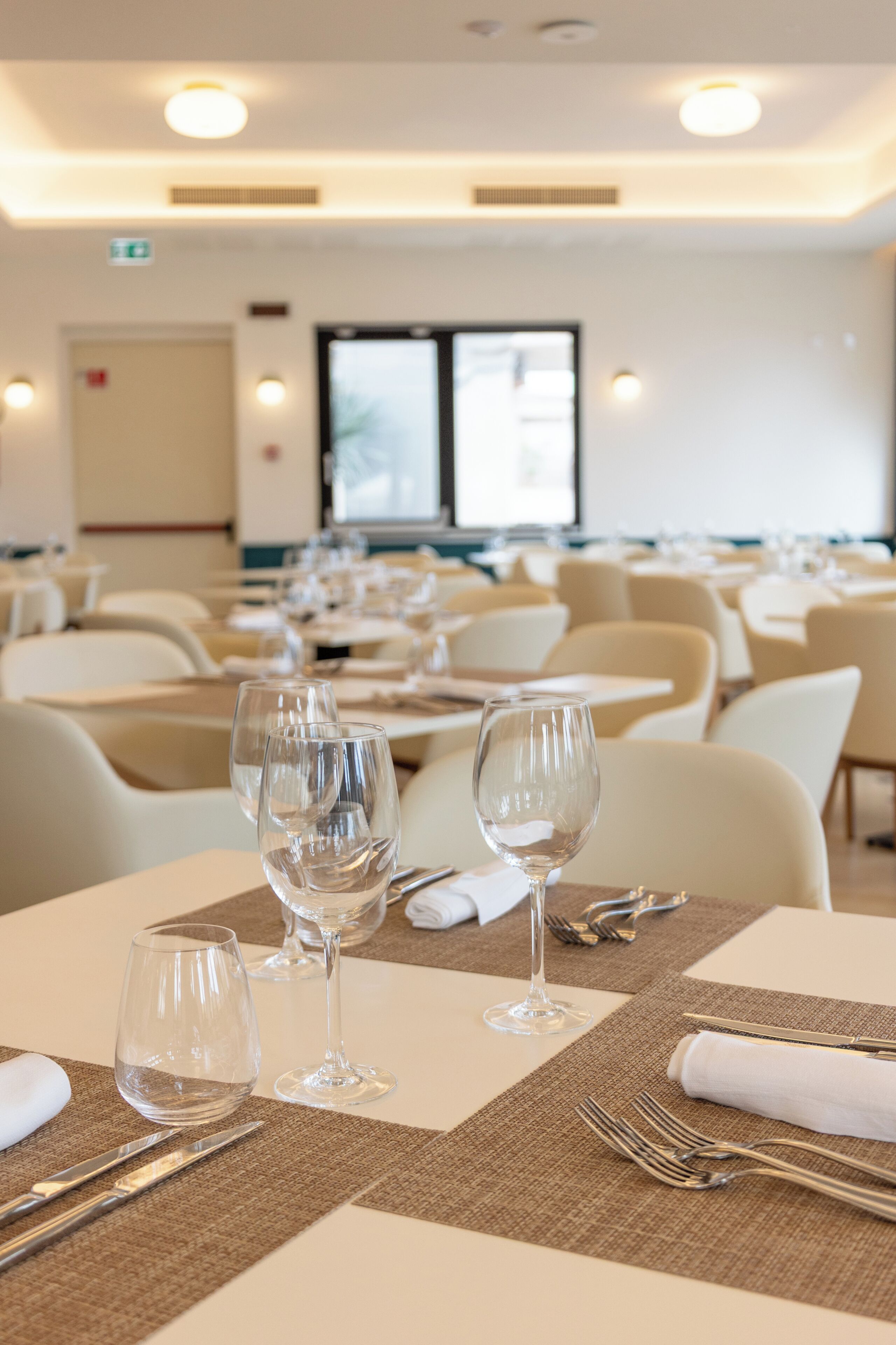 Un espace repas avec des tables mises pour le repas, comprenant des verres à vin et des couverts.