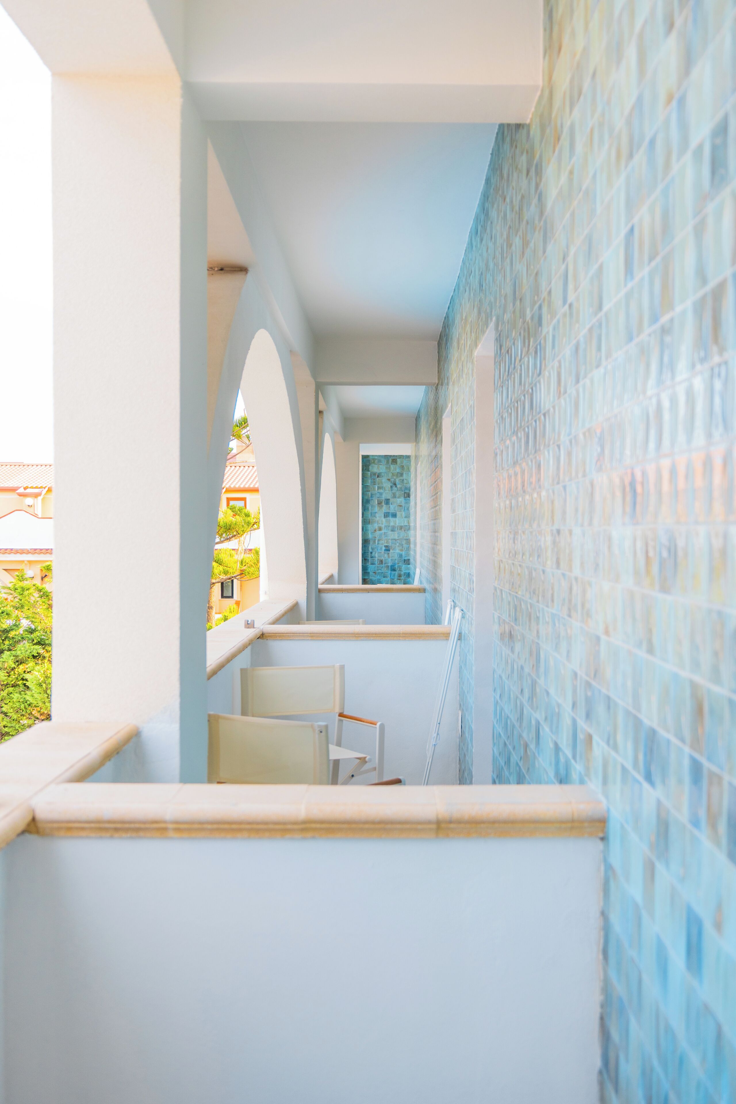 A corridor with a tiled wall and a view of a building outside.
