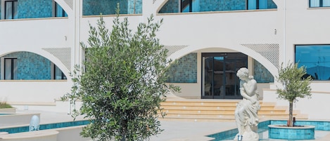 A modern building with a pool area, including a statue and a tree.