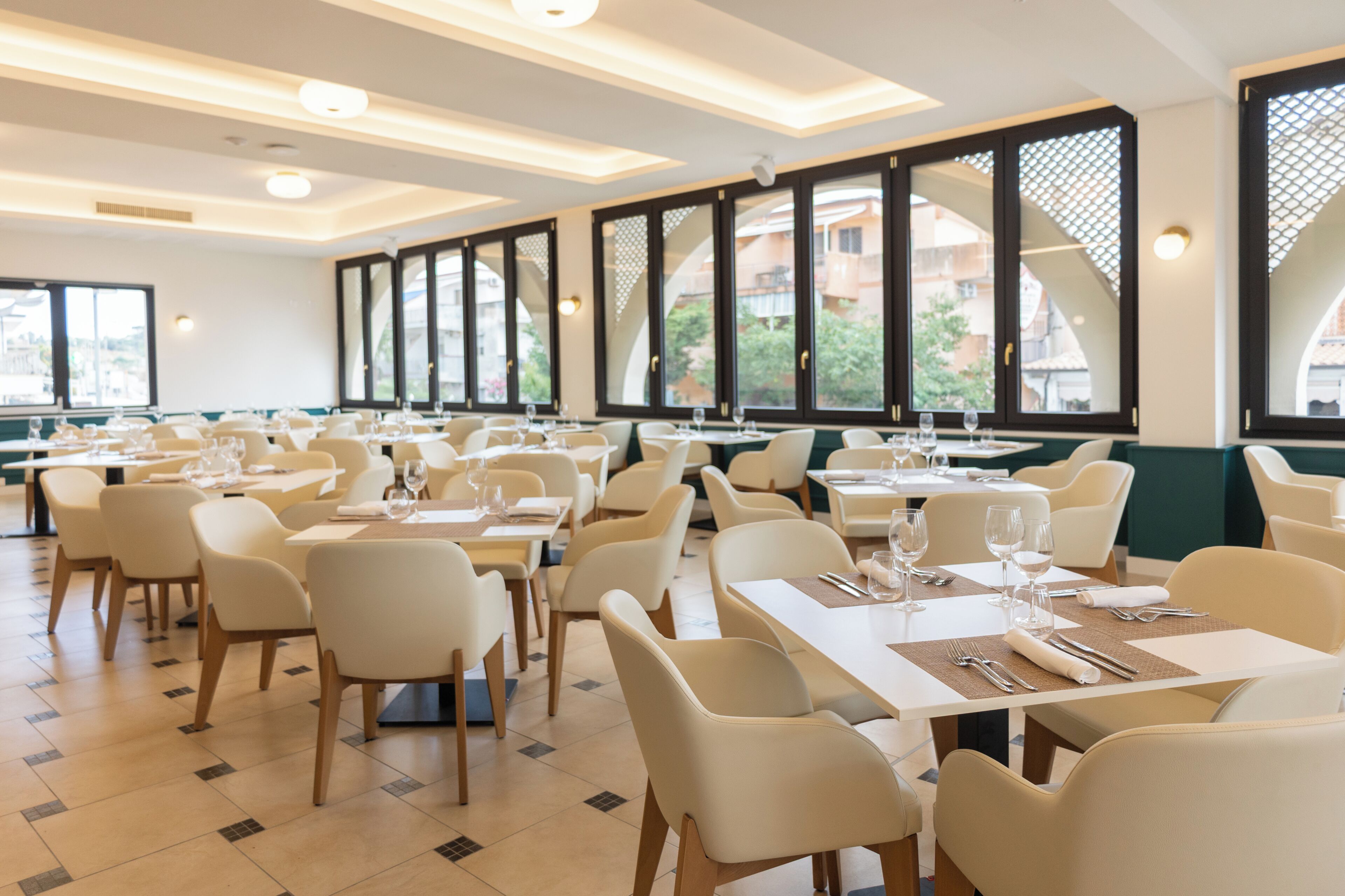 Un restaurante con varias mesas y sillas, grandes ventanales y vistas a edificios.