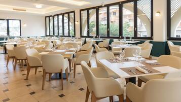 Un restaurante con varias mesas y sillas, grandes ventanales y vistas a edificios.