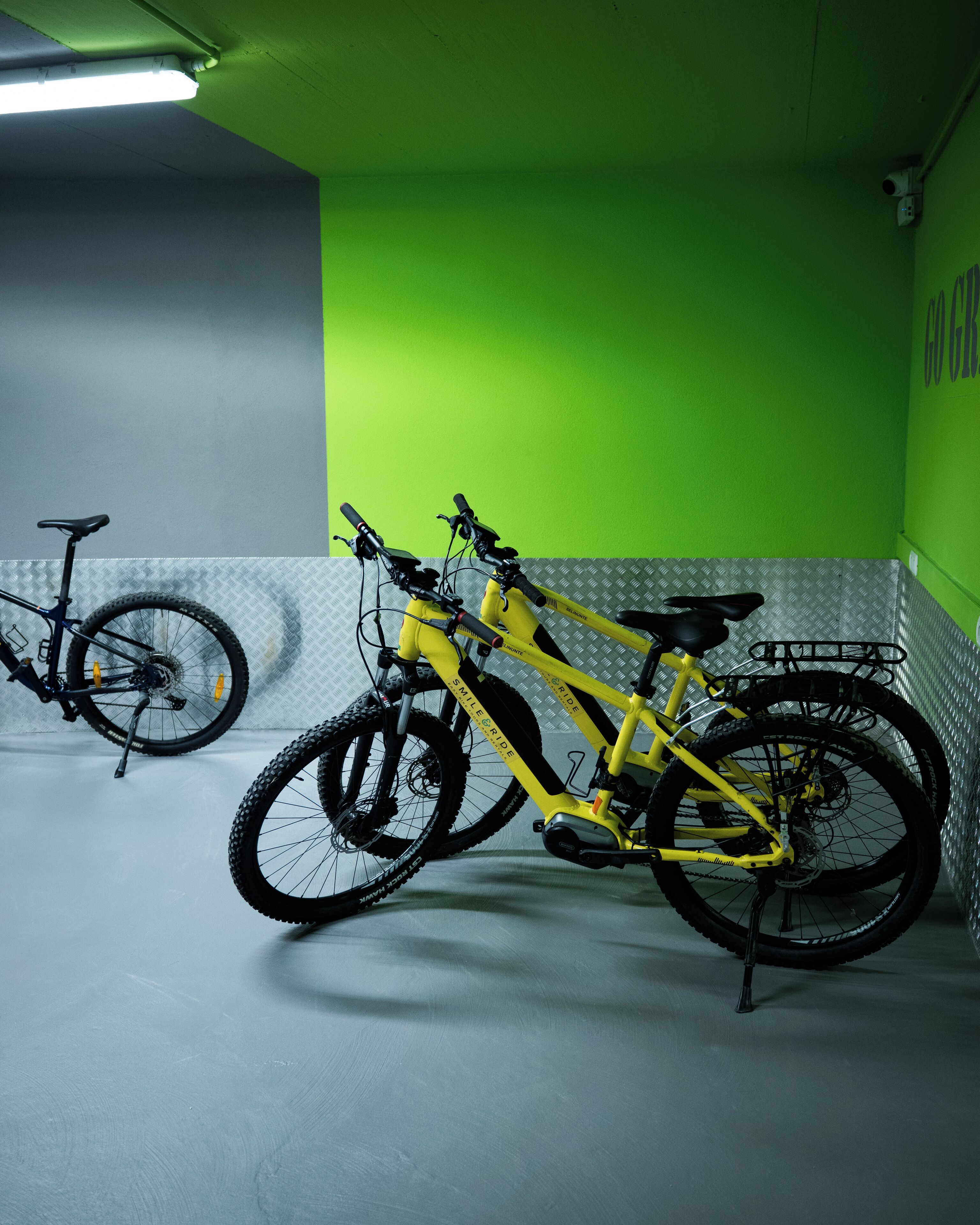 Ein Fahrradabstellraum mit zwei Fahrrädern, einem gelben und einem schwarzen, in einem Zimmer mit grünen und grauen Wänden.
