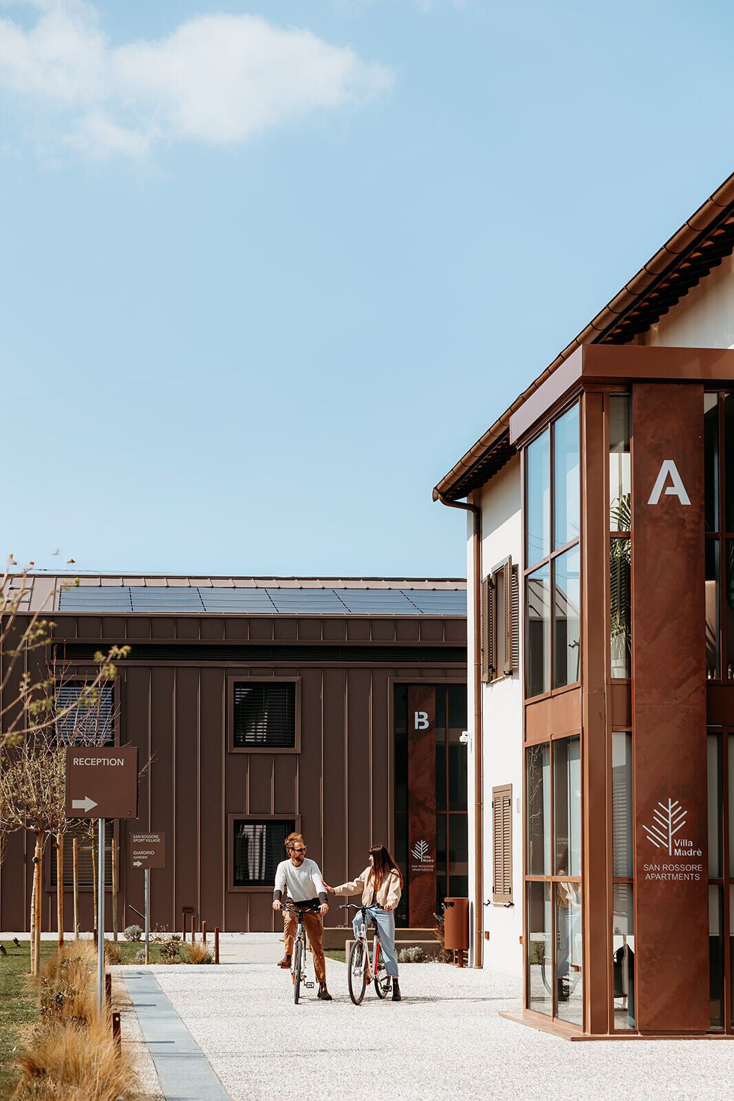 Un bâtiment moderne doté d’un espace d’accueil, d’une enseigne indiquant « Villa Madrès, appartements San Rossore », et d’un ciel dégagé.