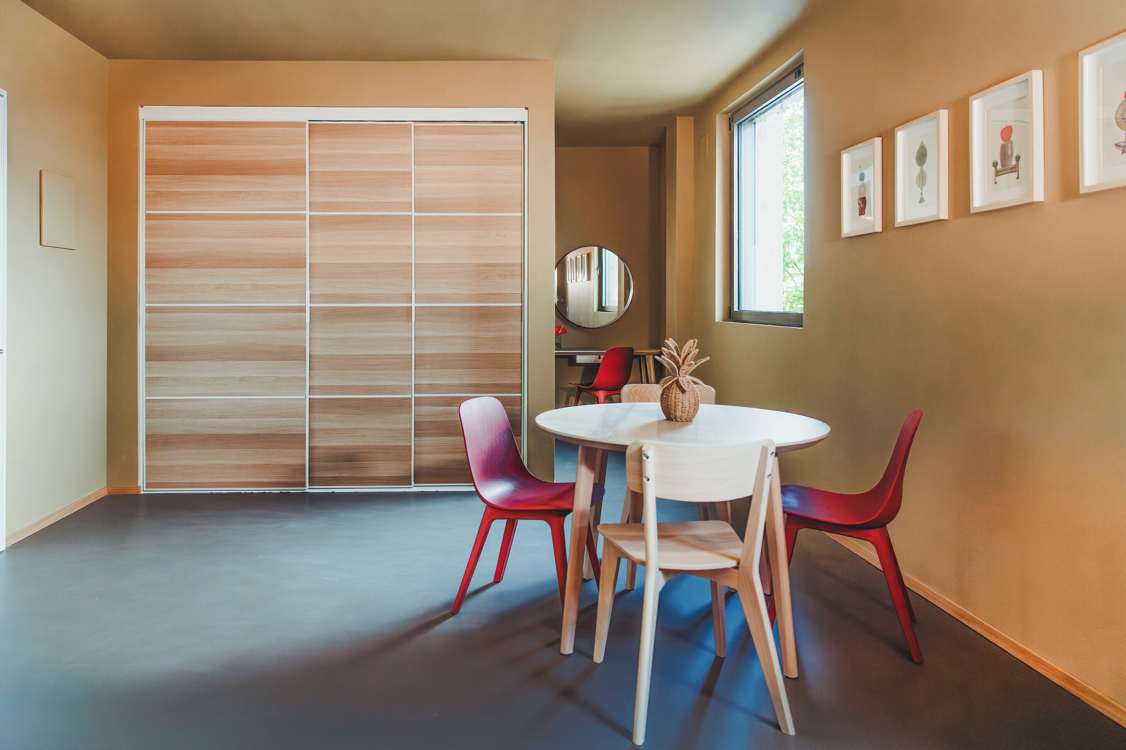 A modern room with a large sliding closet, a round table with chairs, and a window with artwork on the wall.