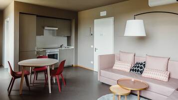 Un apartamento moderno con comedor, kitchenette y sala de estar con sofá y dos mesitas.