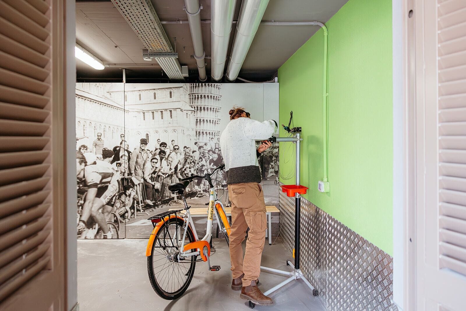 Eine Person steht neben einem Fahrrad in einem Raum mit grüner Wand und einem großen Schwarz-Weiß-Foto.