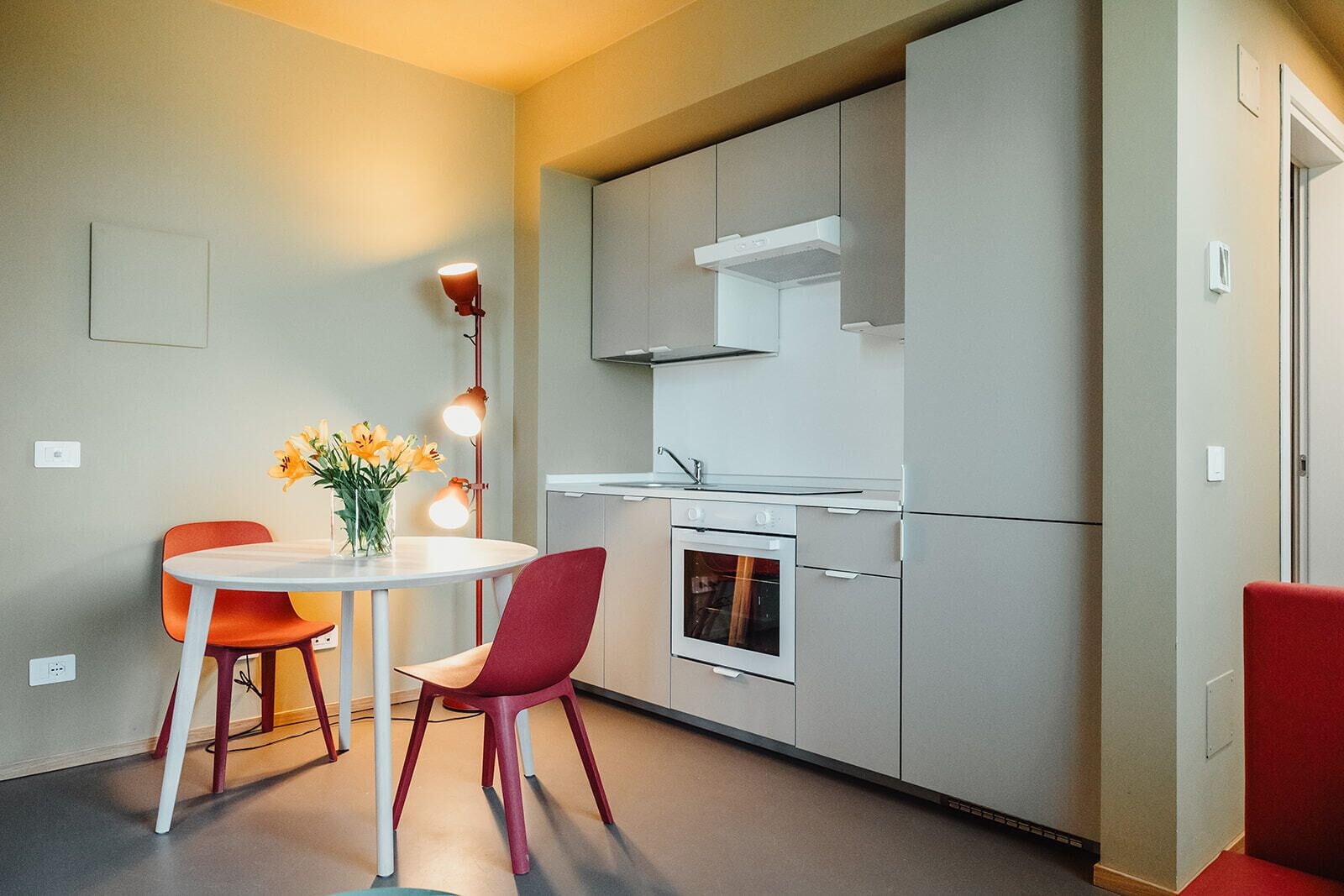 A compact kitchen with a built-in oven, a microwave, and a stove. There is a dining table with two chairs and a vase of flowers.