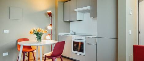 A compact kitchen with a built-in oven, a microwave, and a stove. There is a dining table with two chairs and a vase of flowers.