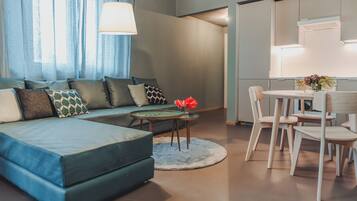 A modern living room with a blue sofa, a small round table with a vase, and a dining area with white chairs.