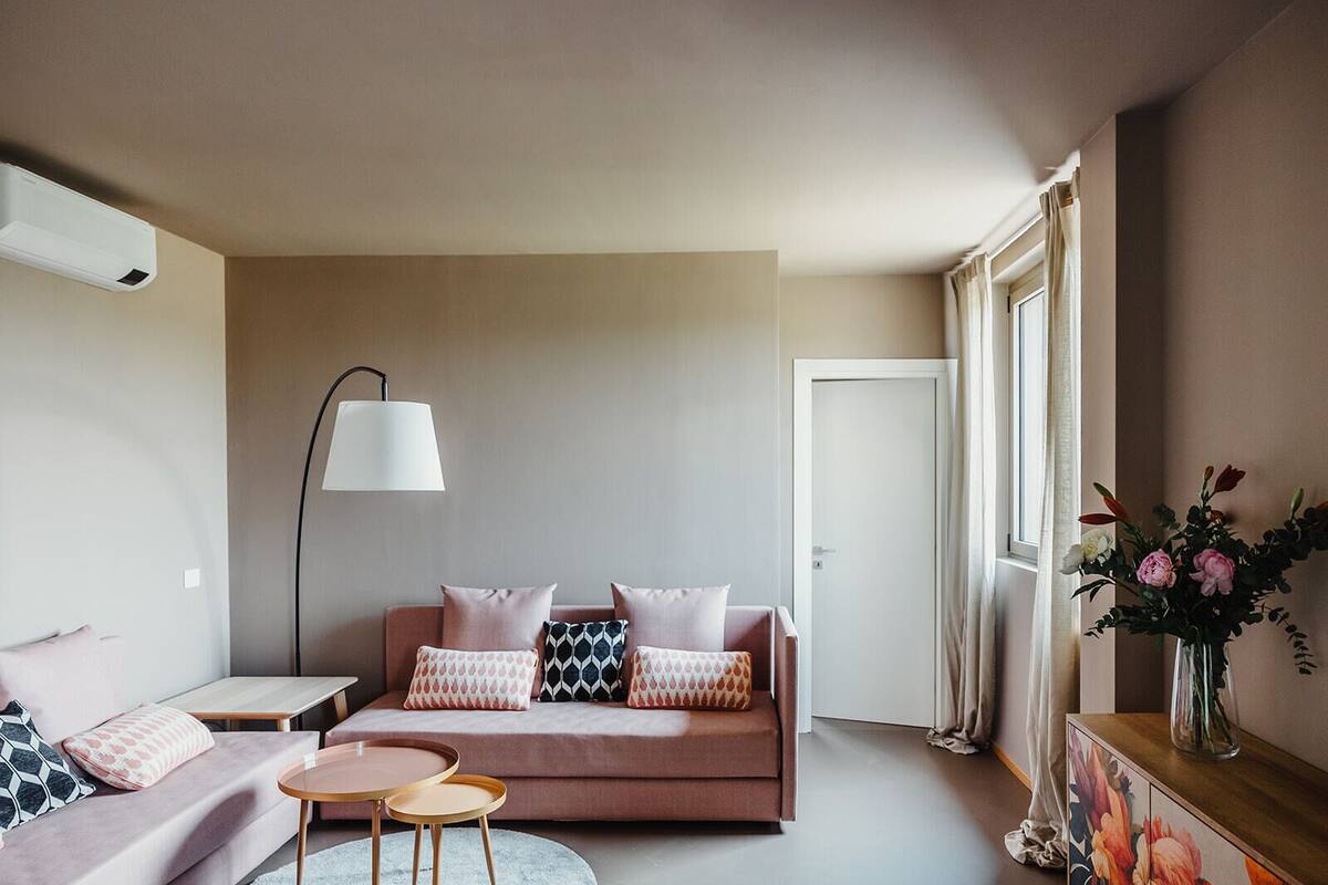 Ein modernes Wohnzimmer mit einer Couch, zwei Beistelltischen, einer Stehlampe und einem Blumenstrauß.