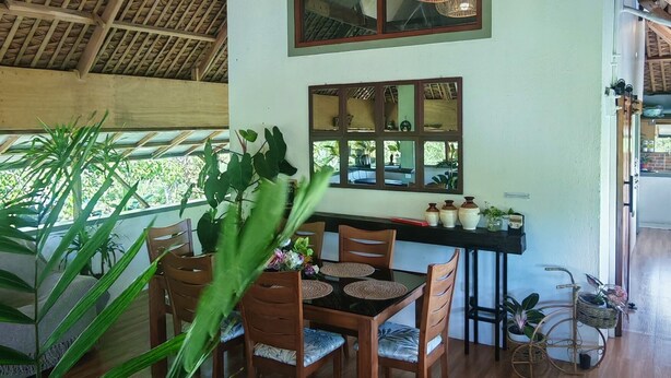 A spacious dining area with wooden furniture, hanging wicker chandeliers, and large windows allowing natural light.