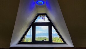 A triangular skylight with a view of a landscape, including trees and mountains.