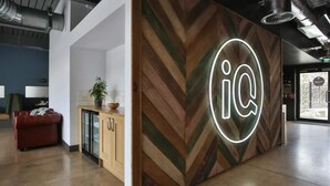 Un espace d’accueil avec un mur en bois disposé en motif chevron, un néon, un canapé en cuir rouge, une petite plante et une vitrine.