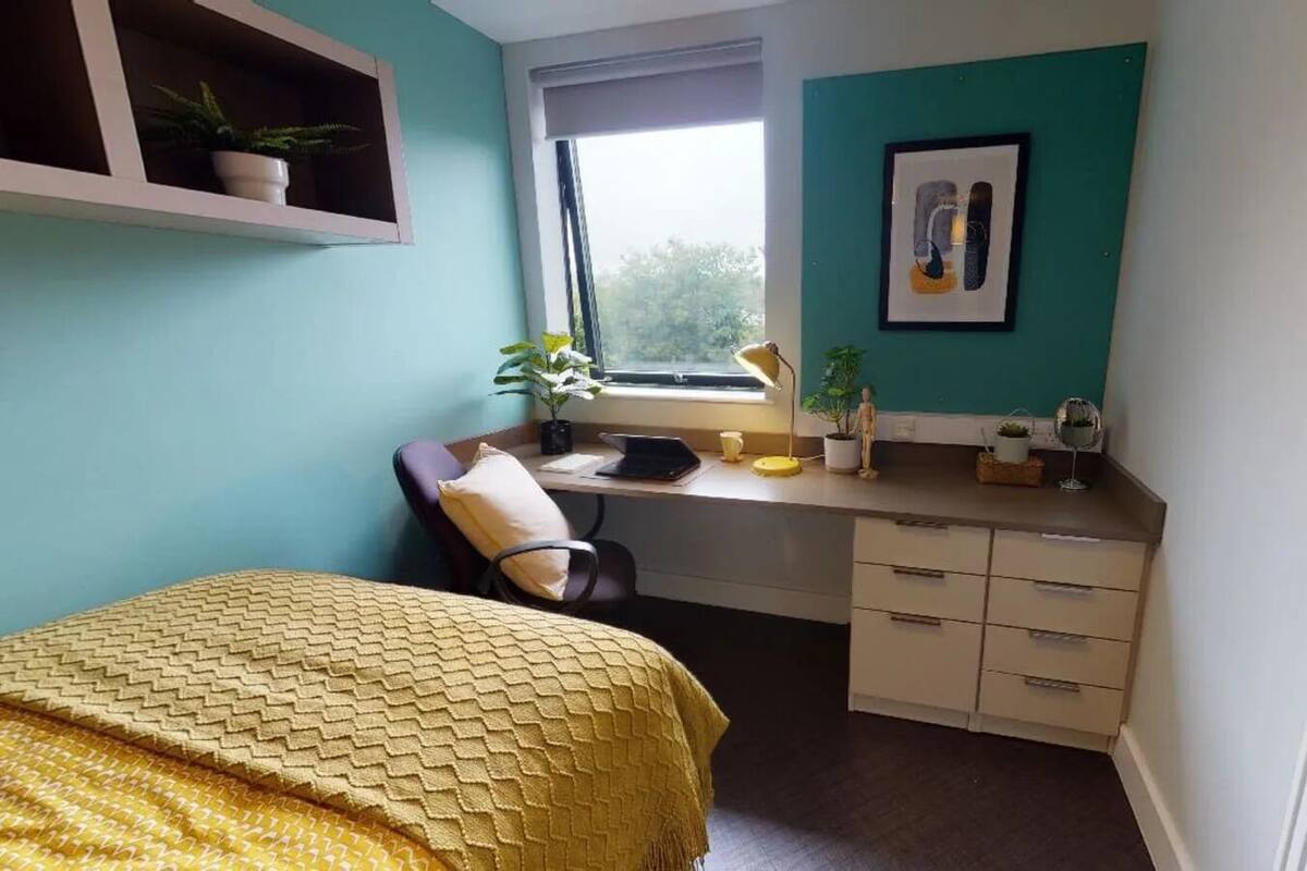 A bedroom with a bed, a desk, a chair, and a window.
