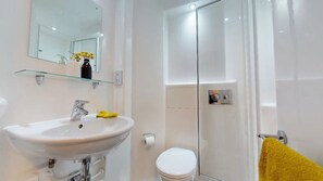 A bathroom with a glass shower enclosure, a white sink with a yellow cloth, and a toilet.
