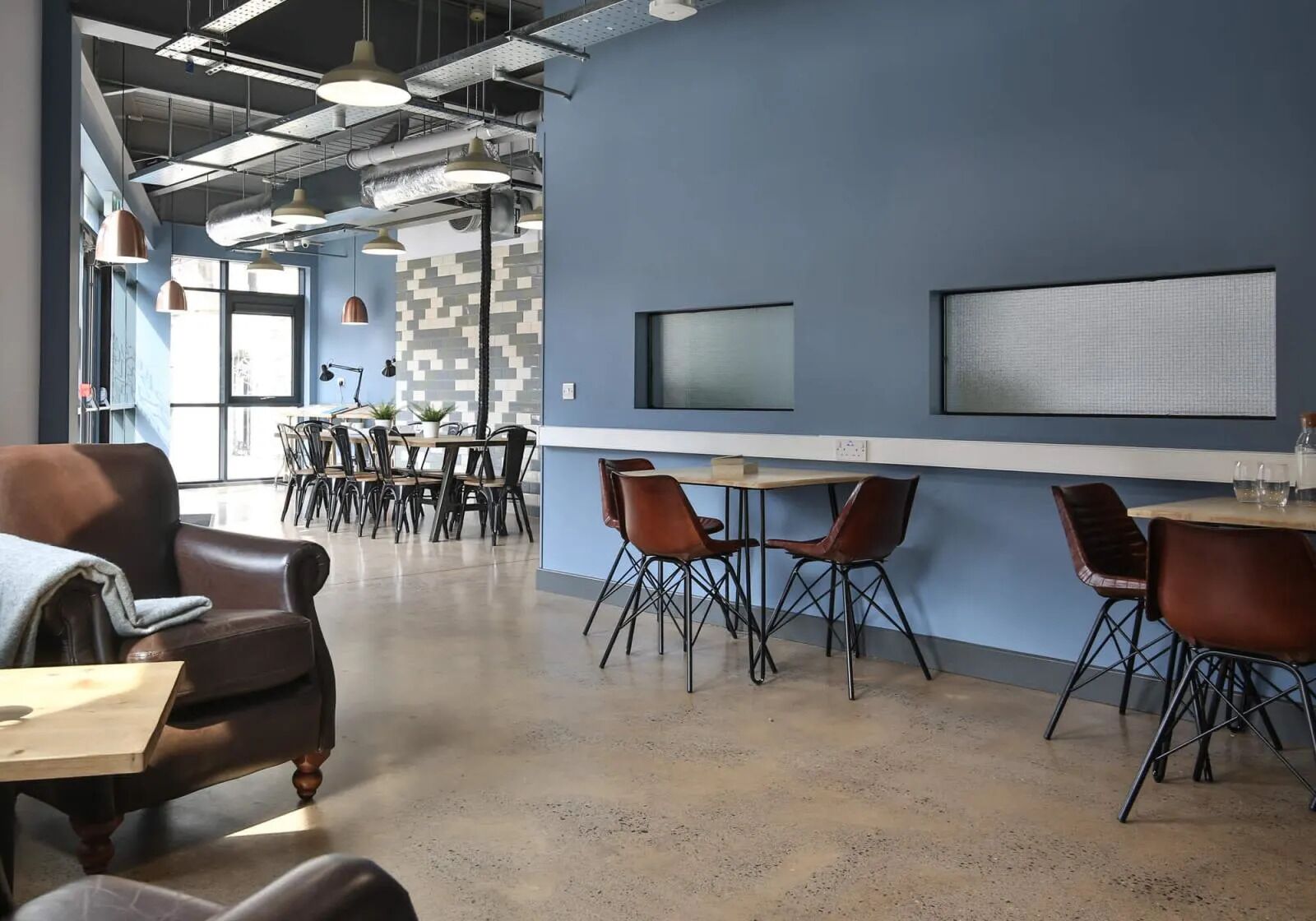 A modern office space with a blue accent wall, multiple tables and chairs, and a large screen.