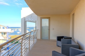 A balcony with a view of the sea, a glass door, and wicker furniture.