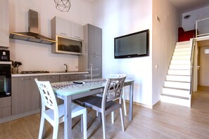A modern kitchen with a dining area, a TV mounted on the wall, and a staircase leading to another level.