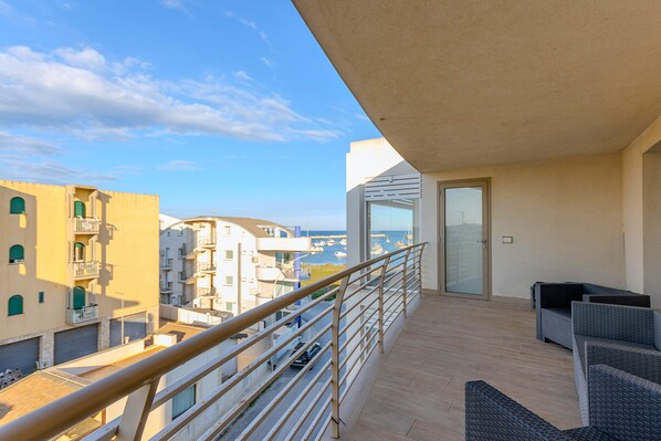 A balcony with a view of the sea, a railing, and a seating area.