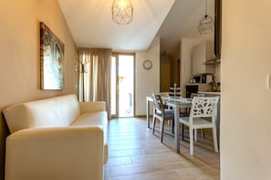 Un salon avec un canapé, une table à manger et des chaises, une horloge au mur et, au fond, un coin cuisine.