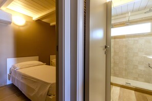 A bedroom with a bed, a bedside table, and a bathroom with a shower and patterned tiles.