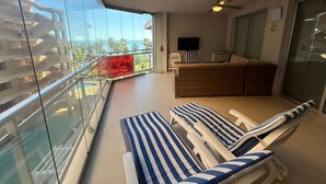 Un balcon doté d’une rambarde en verre, d’un canapé, d’un téléviseur et de fauteuils de relaxation.