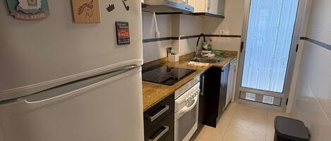 Una cocina moderna con refrigerador, horno y microondas. Cuenta con gabinetes, un lavamanos y una ventana con persianas.