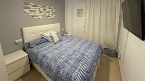 Une chambre à coucher comprenant un lit, une table de chevet, un ventilateur de plafond, un élément de décoration murale, un rideau et un téléviseur fixé au mur.