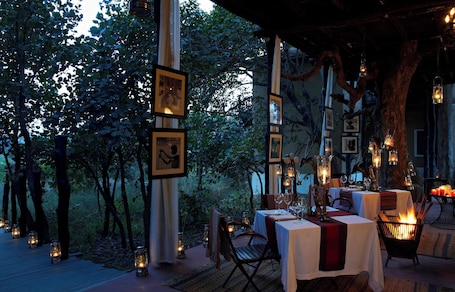 An outdoor dining area with tables set for two, surrounded by trees and lit by lanterns.. Samode Safari Lodge