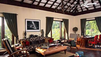 A spacious living room with a high ceiling, a sofa, chairs, a coffee table, and a desk with a lamp.