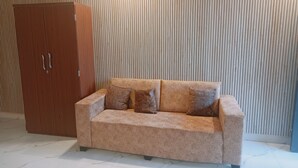 Un sofá color beige con cuatro cojines frente a una pared con líneas verticales. Un armario de madera está a la izquierda.