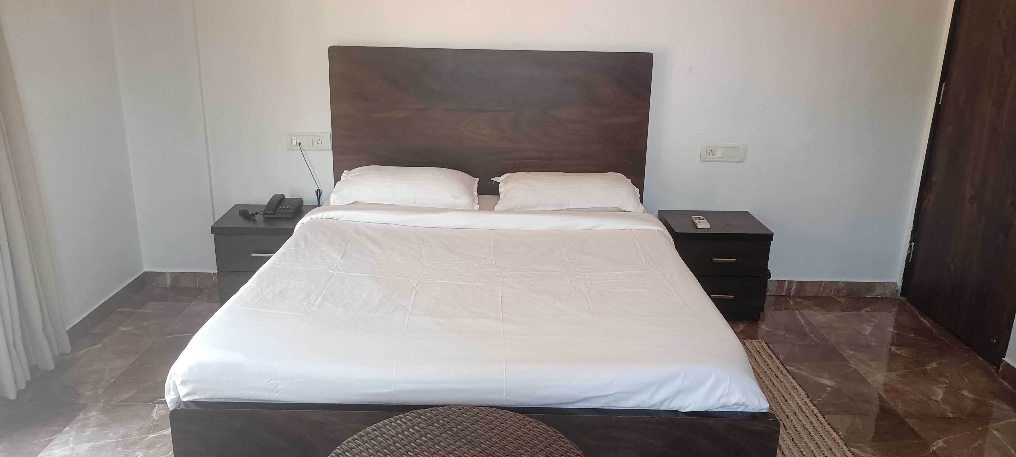 A neatly made bed with a headboard, a bedside table with a phone, and a nightstand with a lamp.