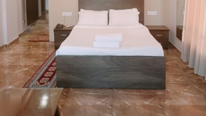 Habitación de hotel con cama, mesitas de noche, un cuadro, unidad de aire acondicionado y alfombra roja.