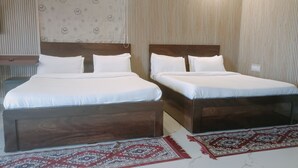 Habitación de hotel con dos camas, un cabecero estampado, una alfombra roja y blanca y un aire acondicionado de pared.