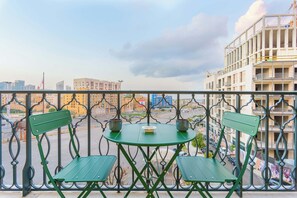 A balcony with a green table and chairs, overlooking a cityscape with buildings and a construction crane.